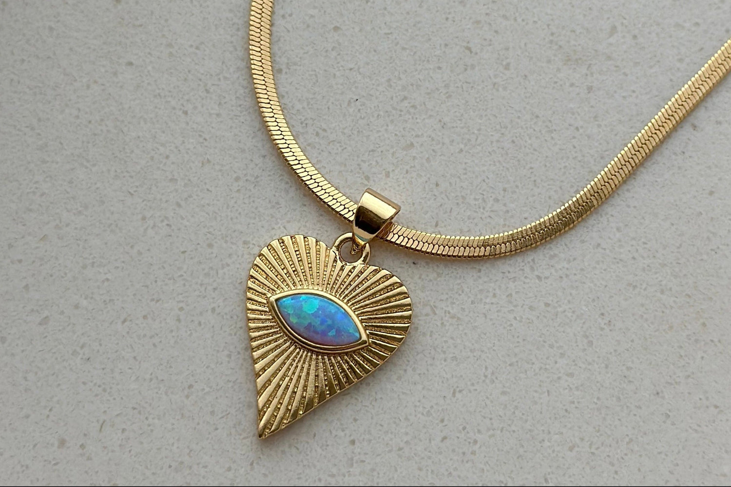 Gold necklace with a heart-shaped pendant featuring a blue stone on a light gray background