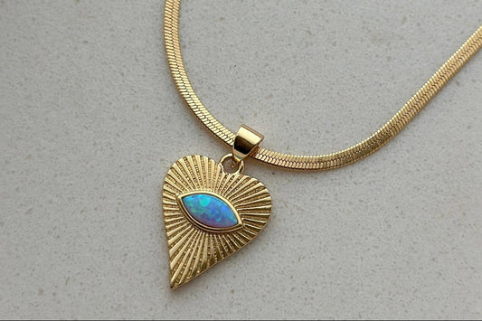 Gold necklace with a heart-shaped pendant featuring a blue stone on a light gray background